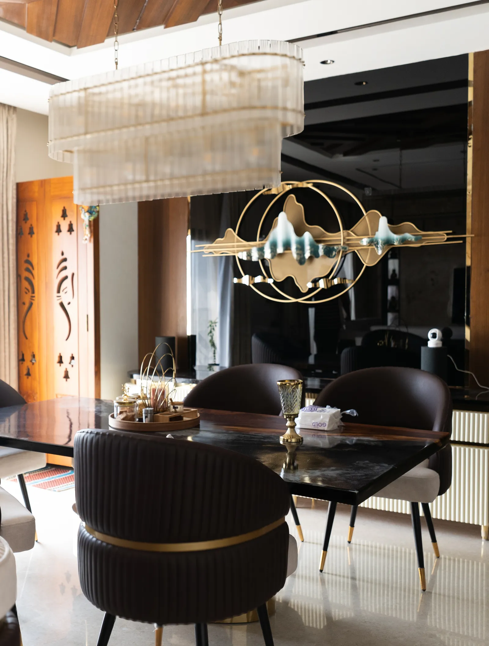 Dining table under a crystal chandelier with gold ring art installation — Abhishek's Residence